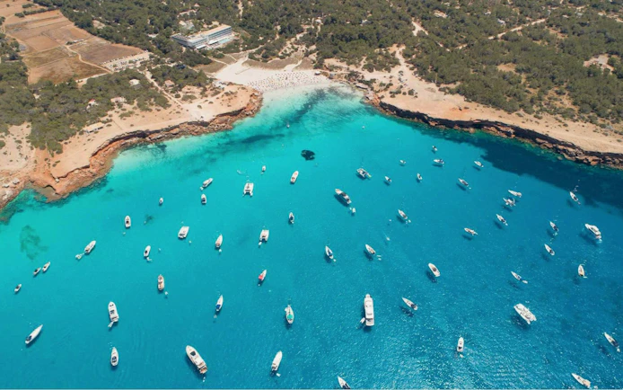 Boats anchored in turquoise waters near Formentera coast, viewed from above.