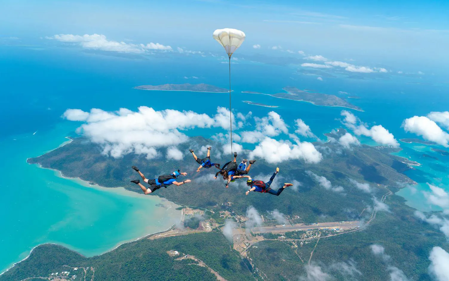 Skydivers in tandem over Airlie Beach with Whitsunday Islands below.