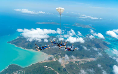 Skydivers in tandem over Airlie Beach with Whitsunday Islands below.