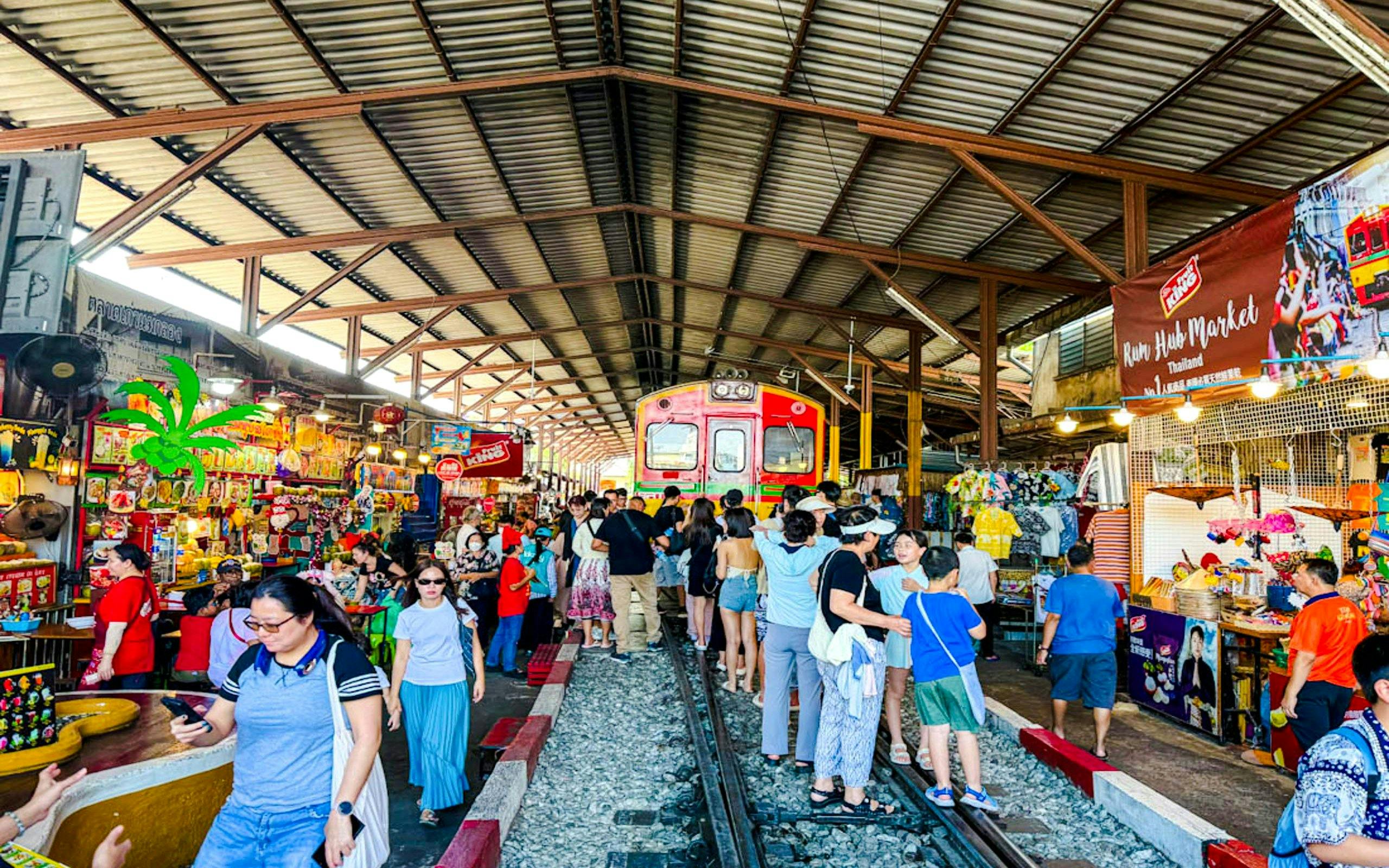 Train passing through Maeklong Railway Market with tourists shopping in Thailand.