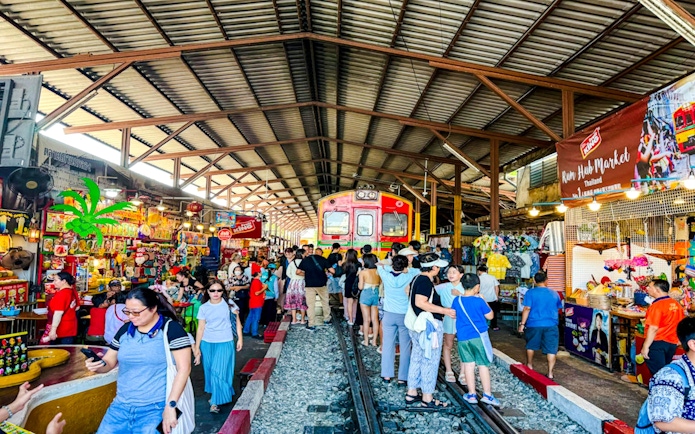 Train passing through Maeklong Railway Market with tourists shopping in Thailand.