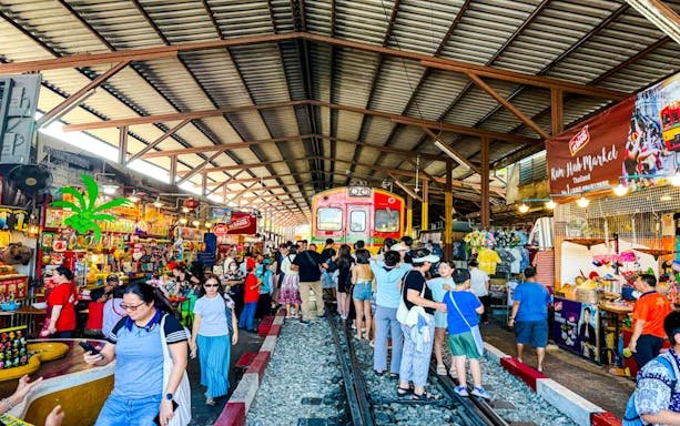 Train passing through Maeklong Railway Market with tourists shopping in Thailand.