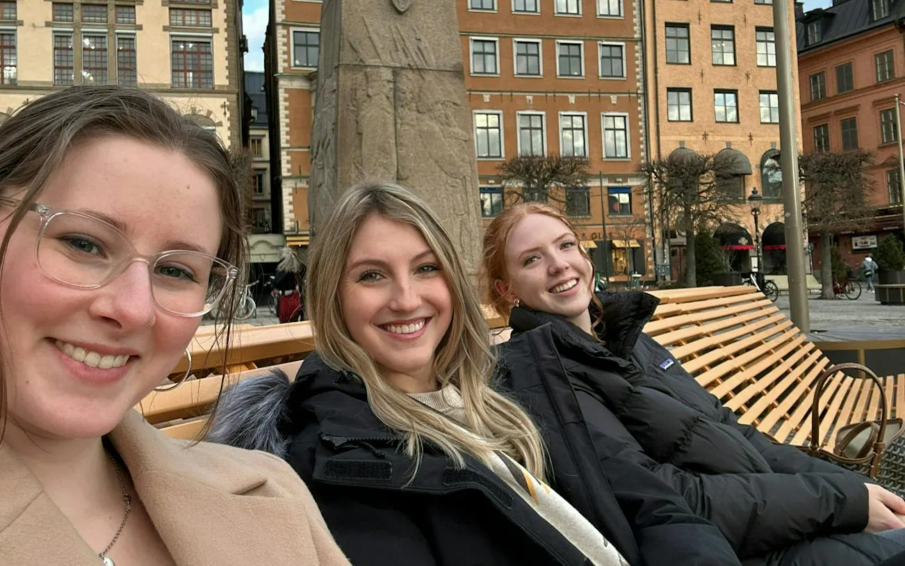 Three people smiling on a bench in Stockholm's historic Gamla Stan district.