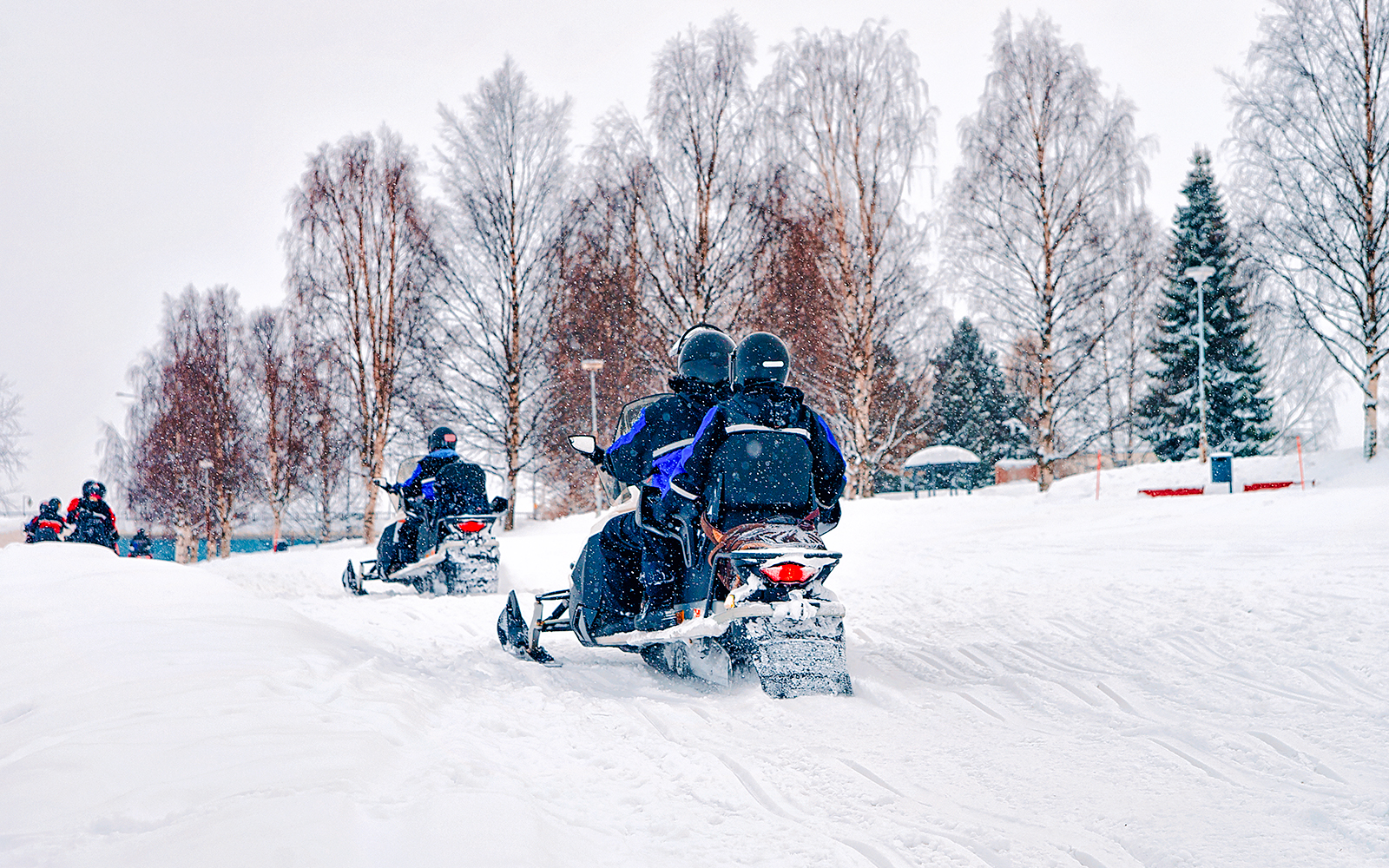 Snowmobilers riding through snowy forest in Lapland during winter.