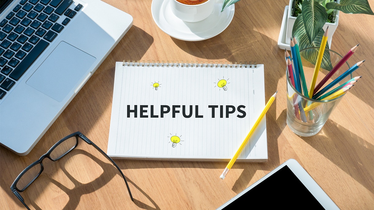 Notebook with "Helpful Tips" text on desk with laptop, coffee, and pencils.
