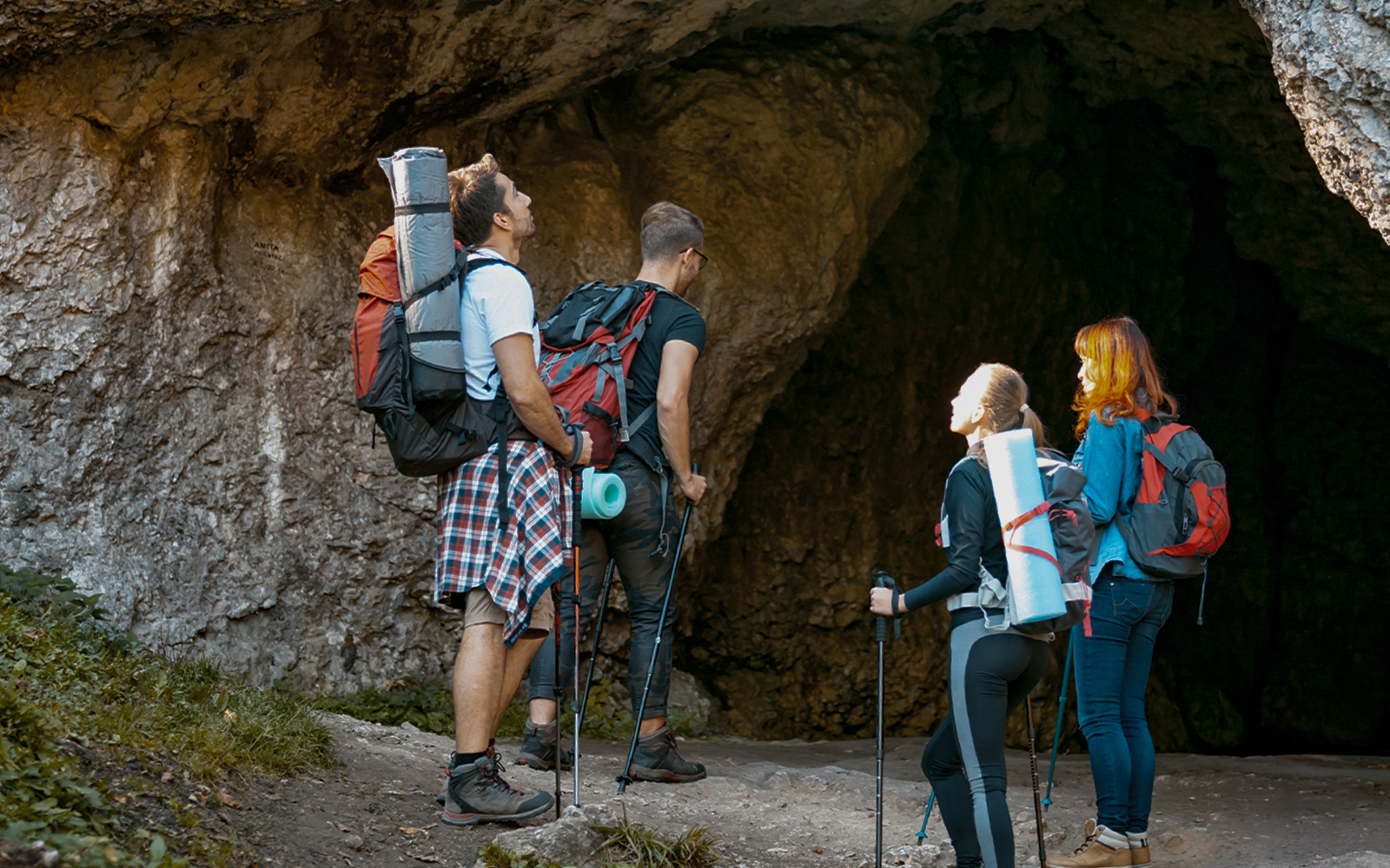 Hikers with backpacks exploring a mountain cave entrance.