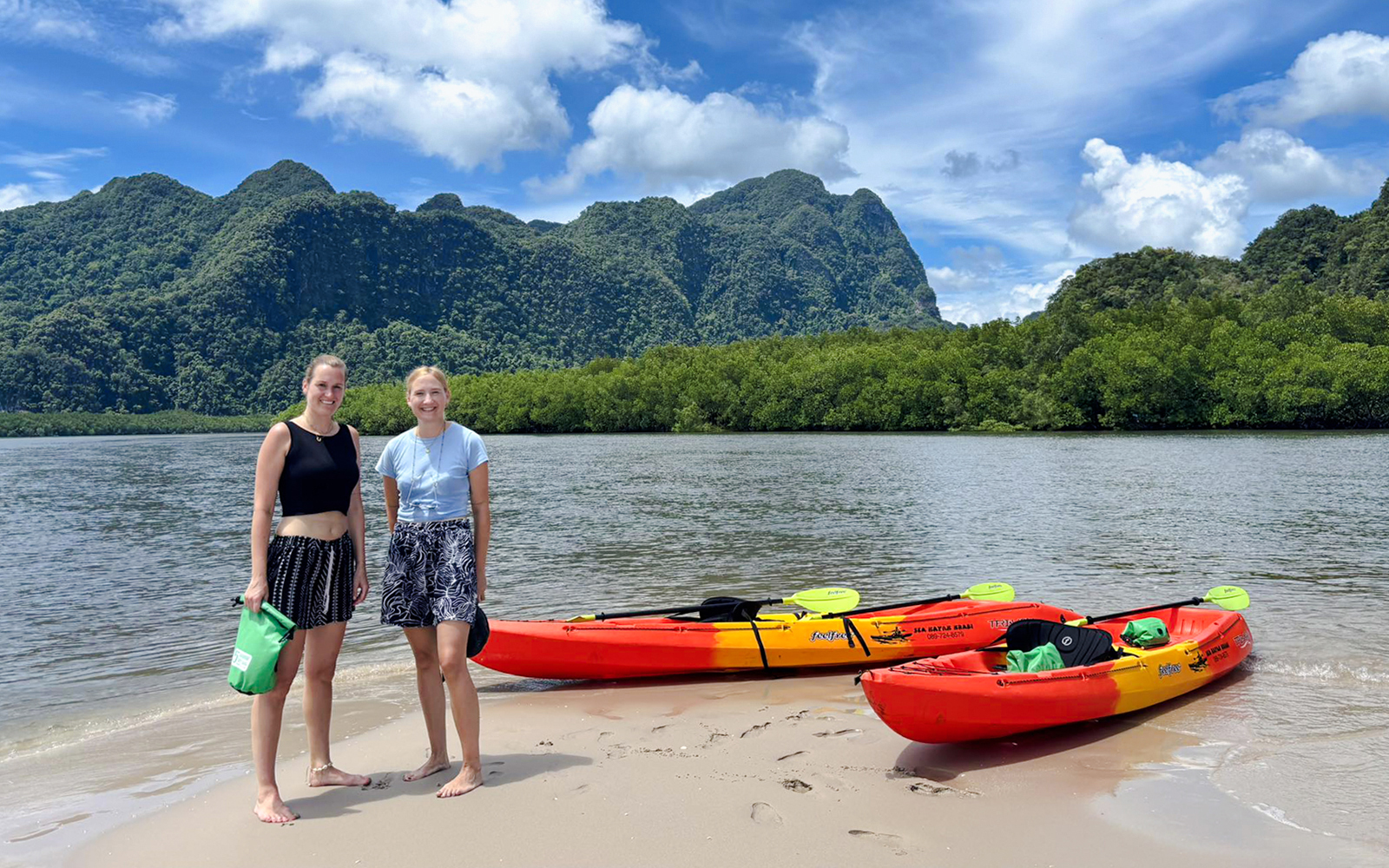 Tourists on Ao Thalane beach with kayaks and limestone cliffs in the background.
