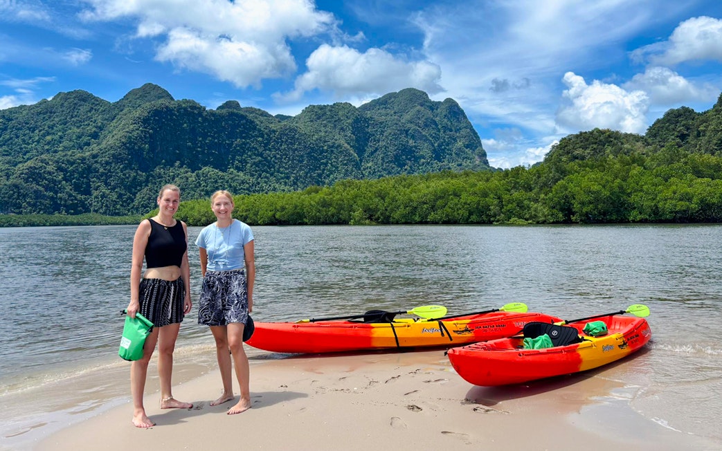 Tourists on Ao Thalane beach with kayaks and limestone cliffs in the background.