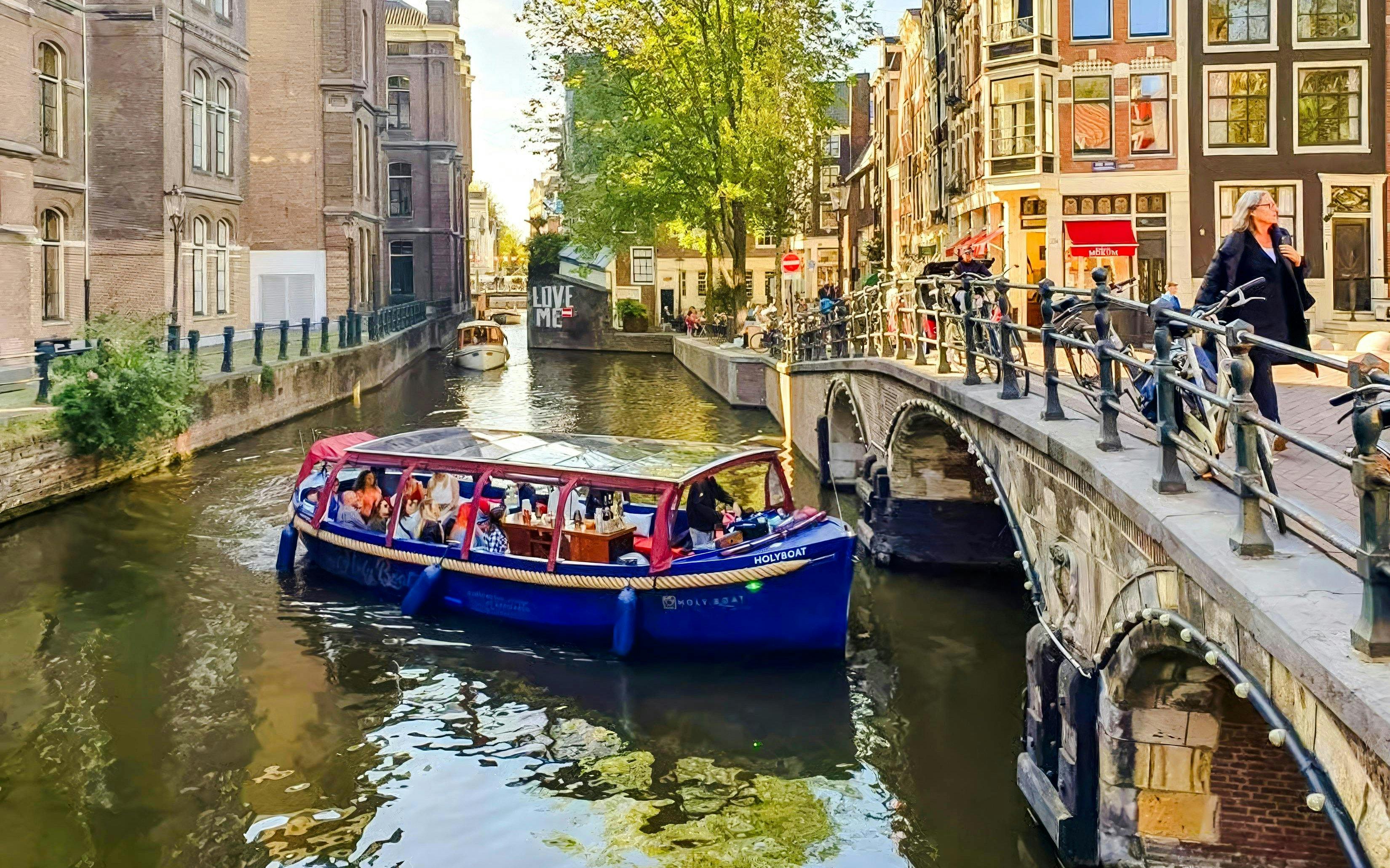 Covered boat cruise on Amsterdam canal with passengers enjoying city views.