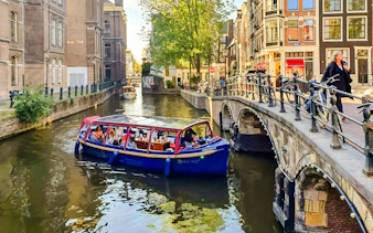 Covered boat cruise on Amsterdam canal with passengers enjoying city views.