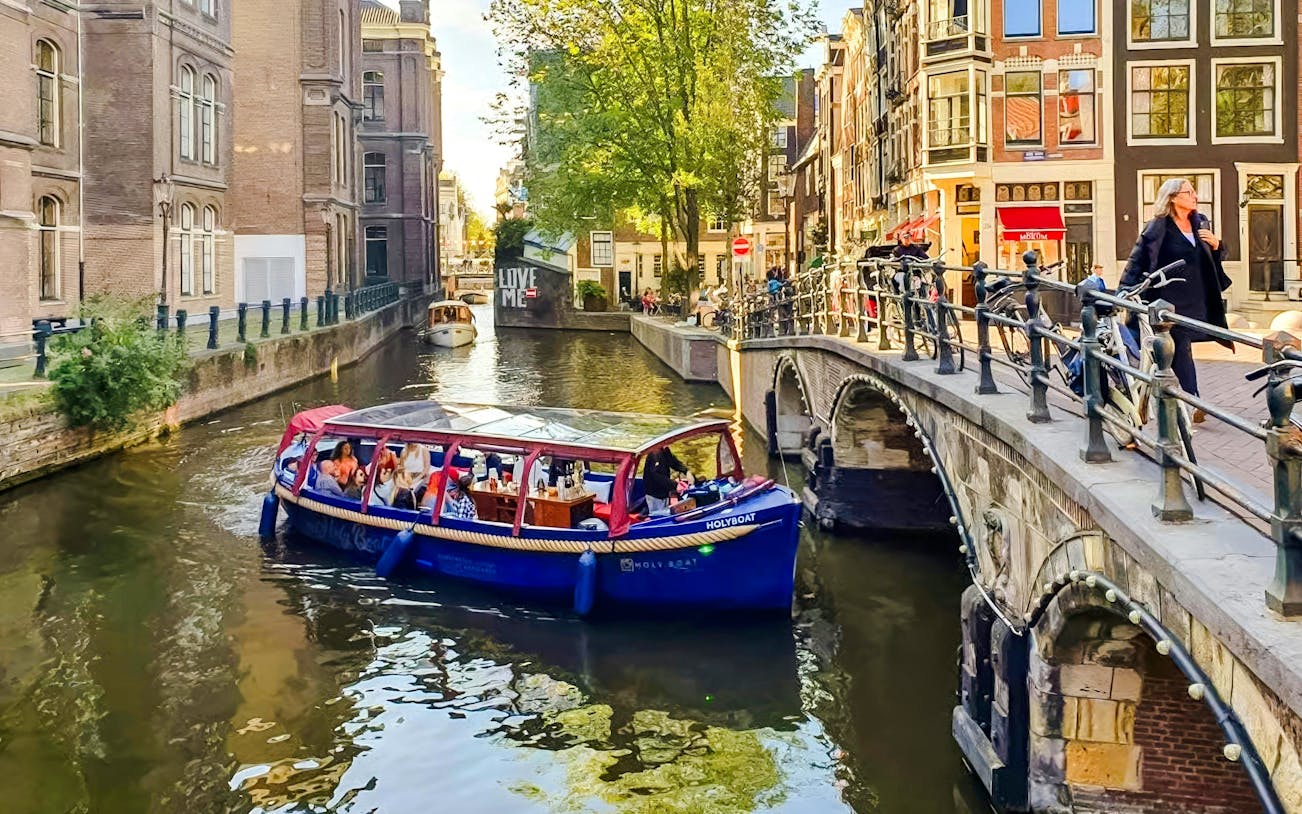 Covered boat cruise on Amsterdam canal with passengers enjoying city views.