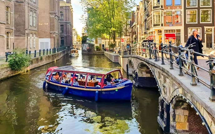 Covered boat cruise on Amsterdam canal with passengers enjoying city views.