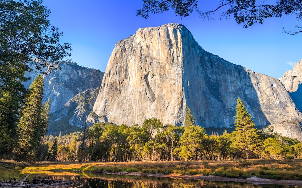 El Capitan rock formation in Yosemite National Park, California, with trees and clear sky.