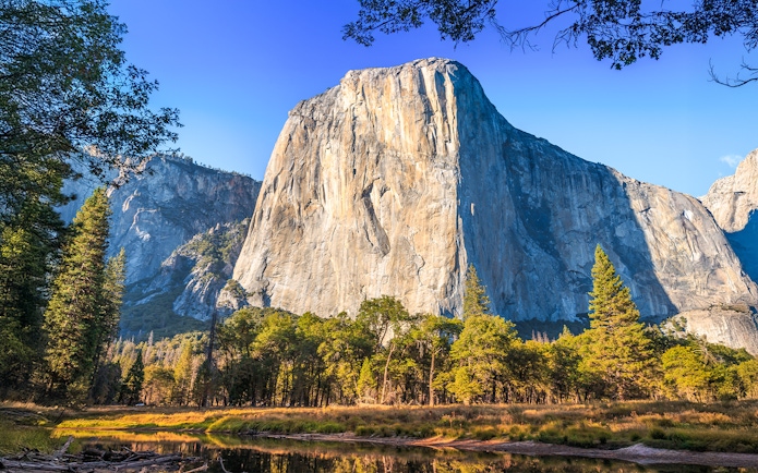 El Capitan rock formation in Yosemite National Park, California, with trees and clear sky.