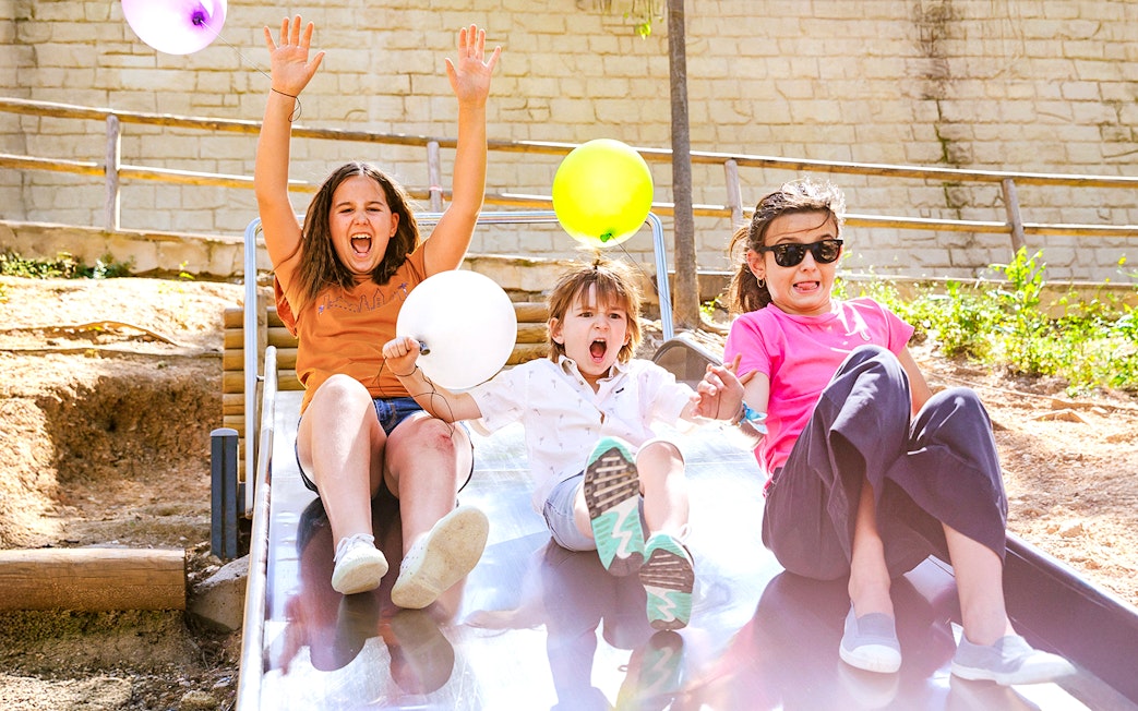 Children enjoying a slide at Poble Espanyol, Barcelona, holding colorful balloons.