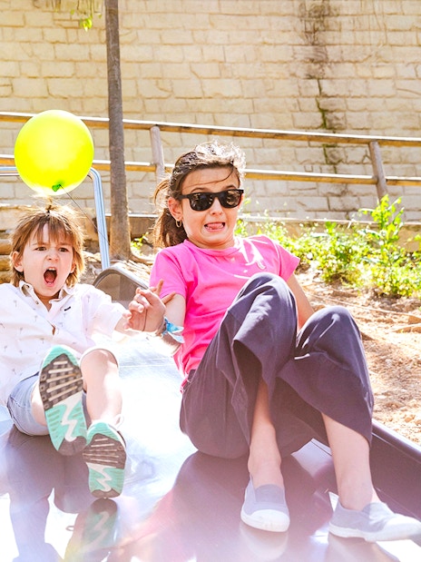 Children enjoying a slide at Poble Espanyol, Barcelona, holding colorful balloons.