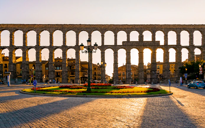 Aqueduct of Segovia with arches and surrounding cityscape at sunset.
