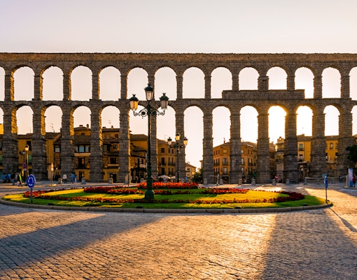 Aqueduct of Segovia with arches and surrounding cityscape at sunset.
