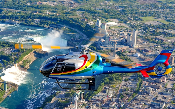 Helicopter flying over Niagara Falls with cityscape in the background.