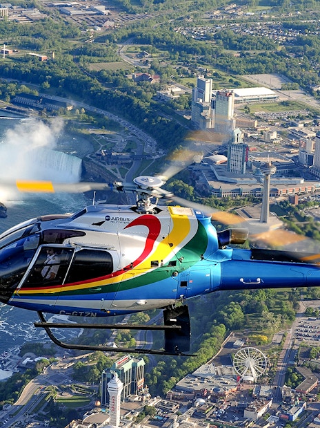 Helicopter flying over Niagara Falls with cityscape in the background.