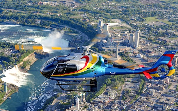 Helicopter flying over Niagara Falls with cityscape in the background.