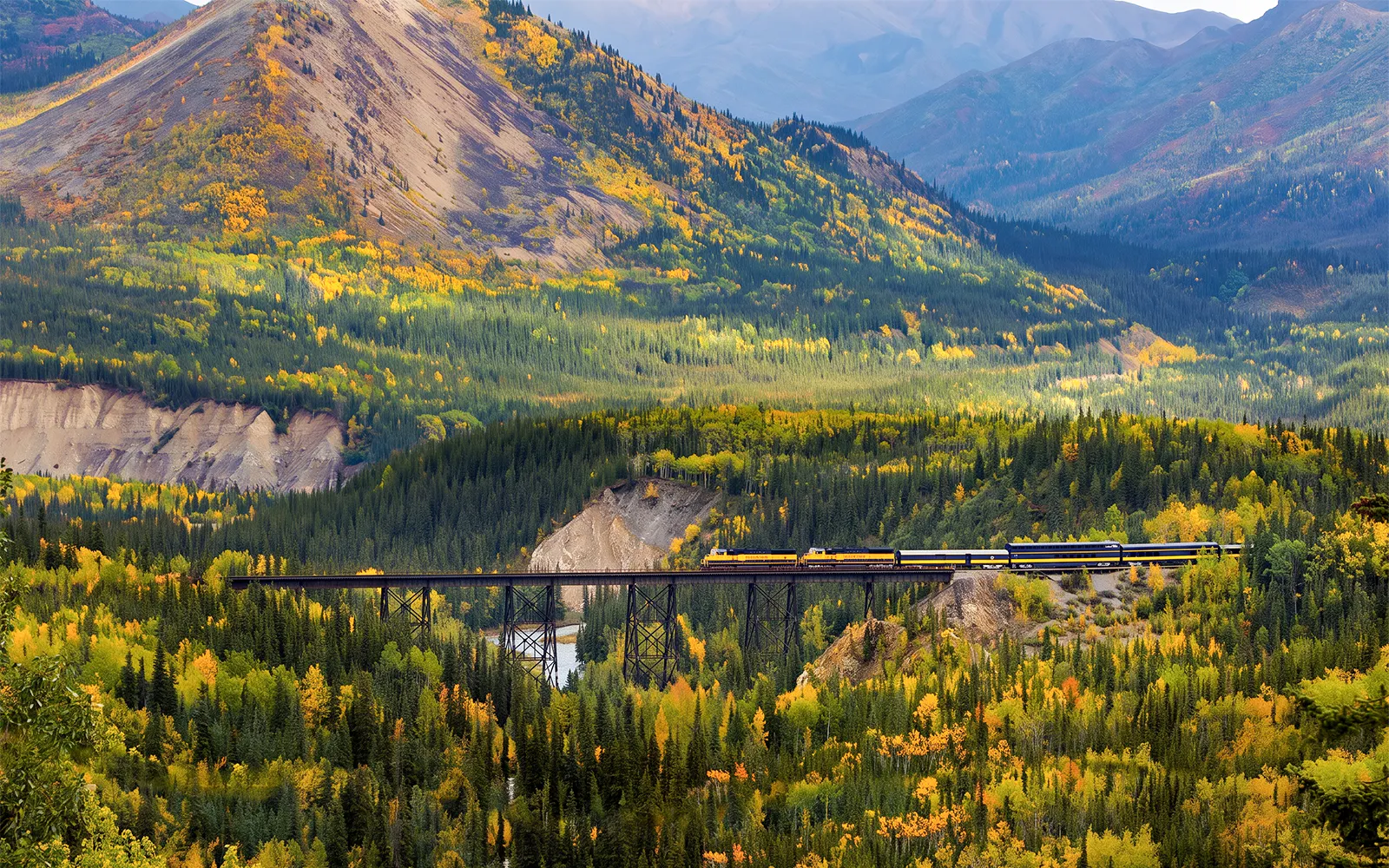 Train crossing a bridge in Alaska's autumn landscape on the Alaska Railroad.
