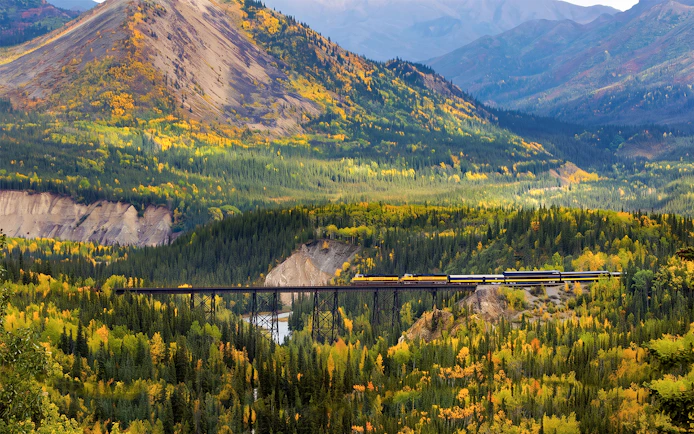 Train crossing a bridge in Alaska's autumn landscape on the Alaska Railroad.