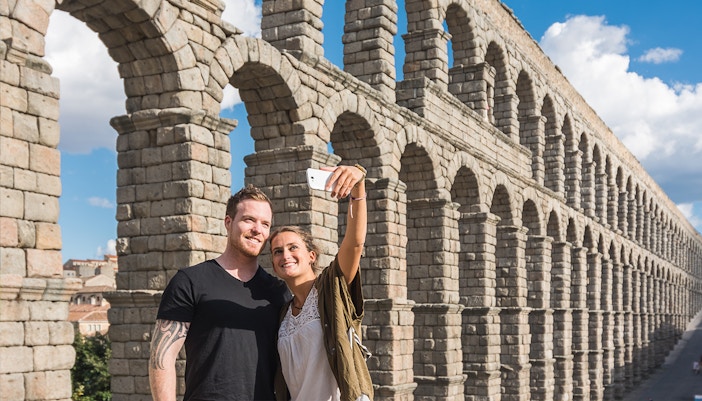 Visitors taking a selfie in front of the Roman Aqueduct, Segovia, Spain.