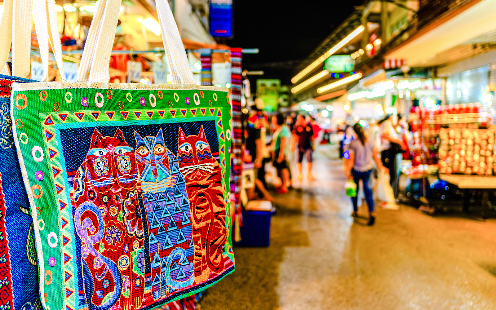 Colorful embroidered bag with cat design at a bustling night market in Thailand.