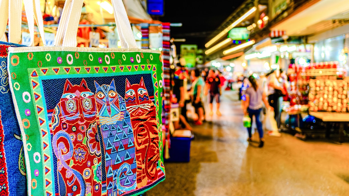 Colorful embroidered bag with cat design at a bustling night market in Thailand.