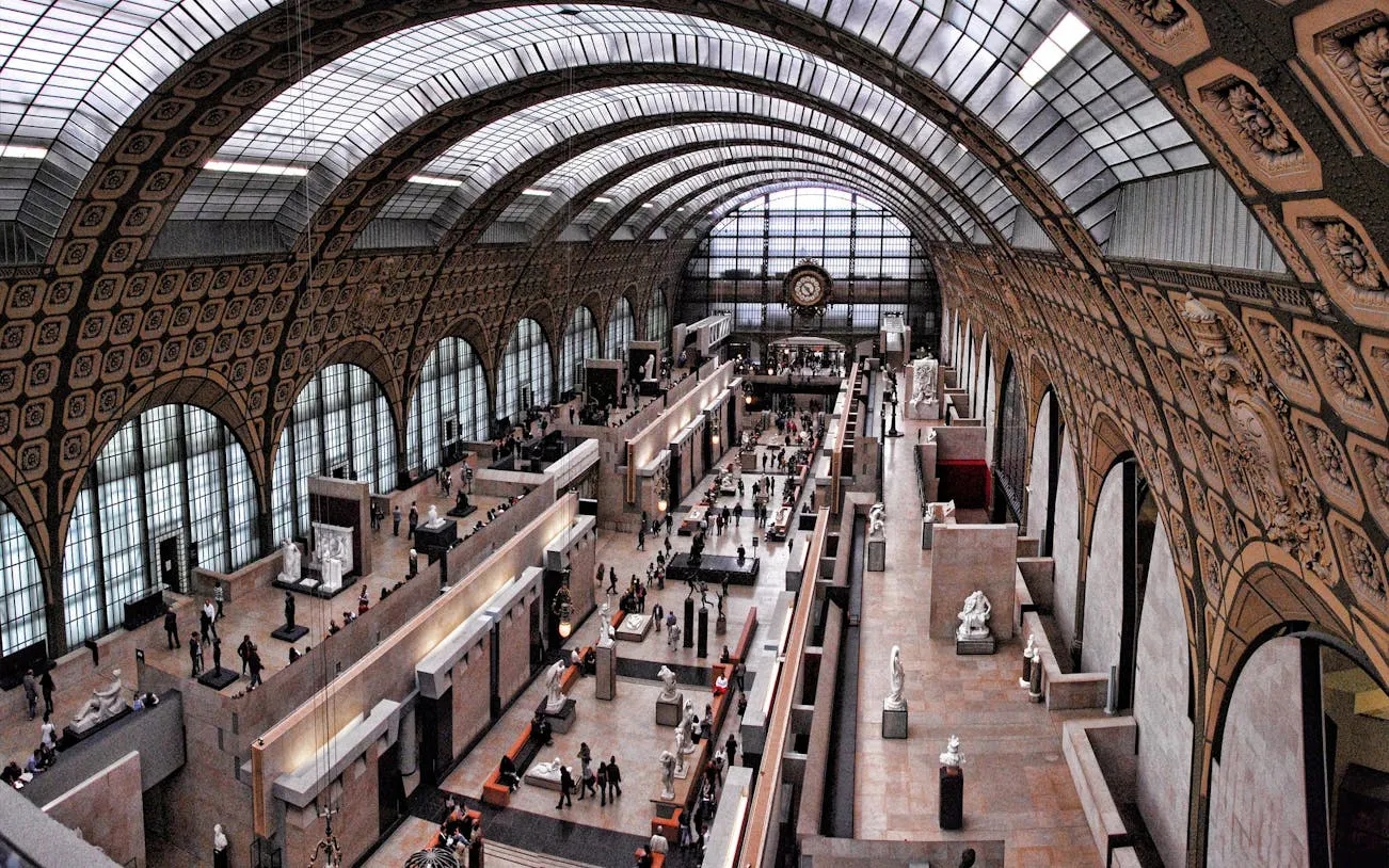 Interior view of Orsay Museum's main hall with sculptures and visitors in Paris.