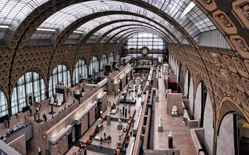 Interior view of Orsay Museum's main hall with sculptures and visitors in Paris.