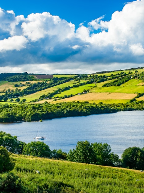 Loch Ness with sailboat, surrounded by lush hills and fields, view from Glencoe and the Highlands.