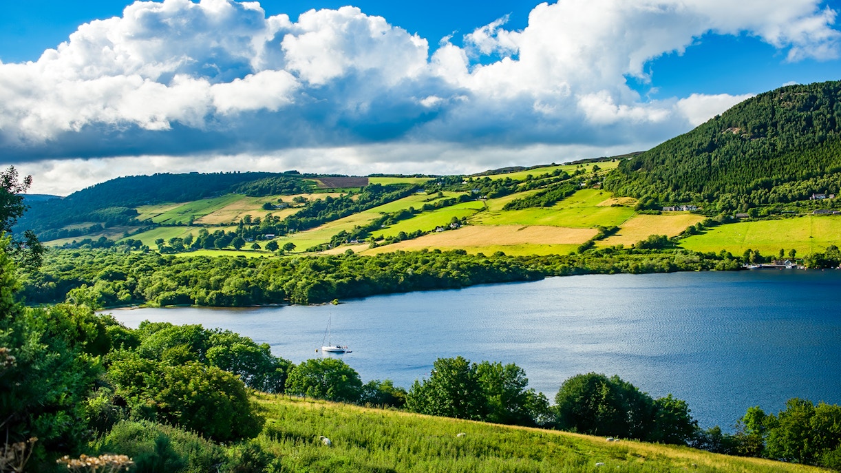 Loch Ness with sailboat, surrounded by lush hills and fields, view from Glencoe and the Highlands.