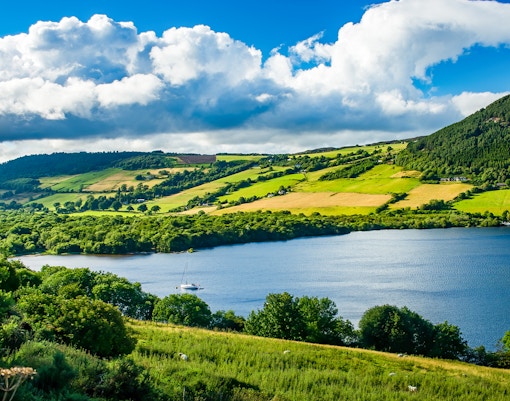 Loch Ness with sailboat, surrounded by lush hills and fields, view from Glencoe and the Highlands.