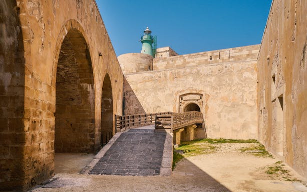 Maniace Castle stone archway and pathway with lighthouse in Syracuse, Italy.
