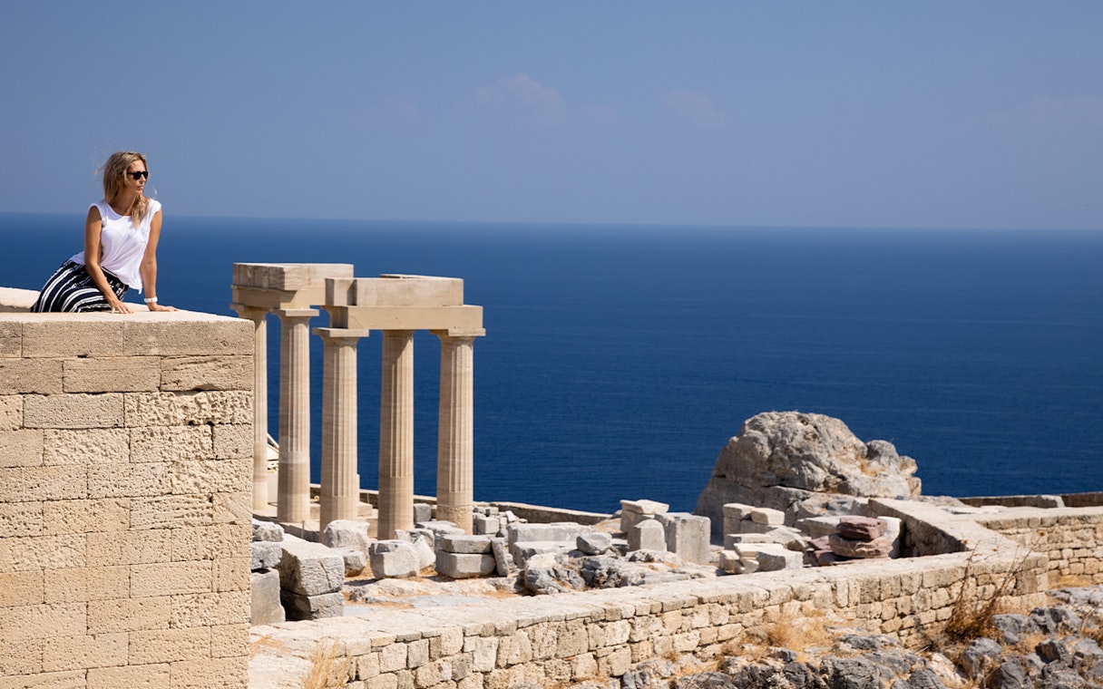 Visitor at the Acropolis of Lindos with ancient columns and sea view in Rhodes, Greece.