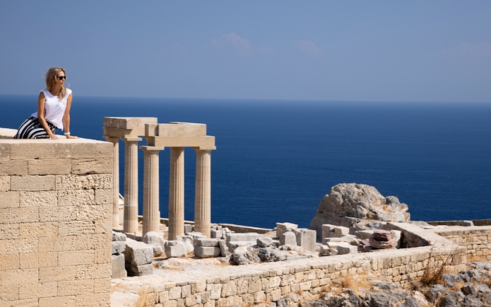 Visitor at the Acropolis of Lindos with ancient columns and sea view in Rhodes, Greece.