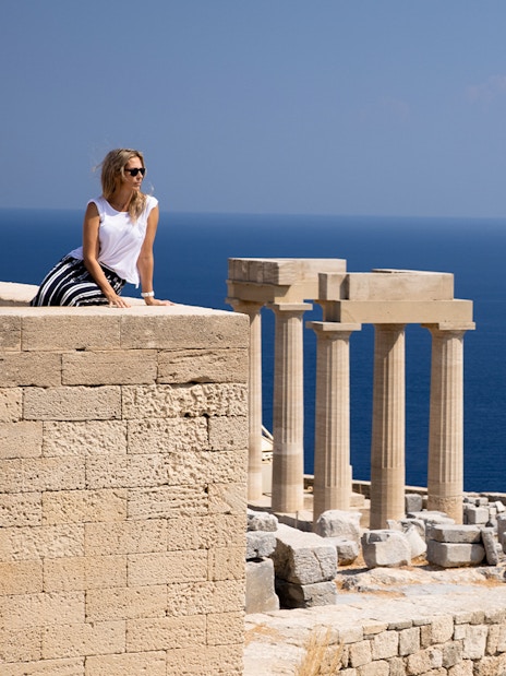 Visitor at the Acropolis of Lindos with ancient columns and sea view in Rhodes, Greece.