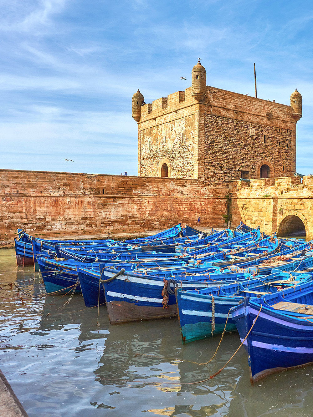 Blue fishing boats docked near Sqala du Port tower in Essaouira, Morocco.
