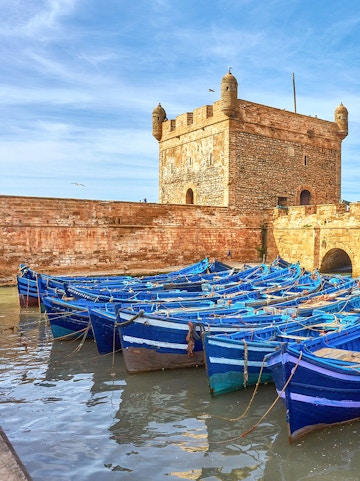 Blue fishing boats docked near Sqala du Port tower in Essaouira, Morocco.