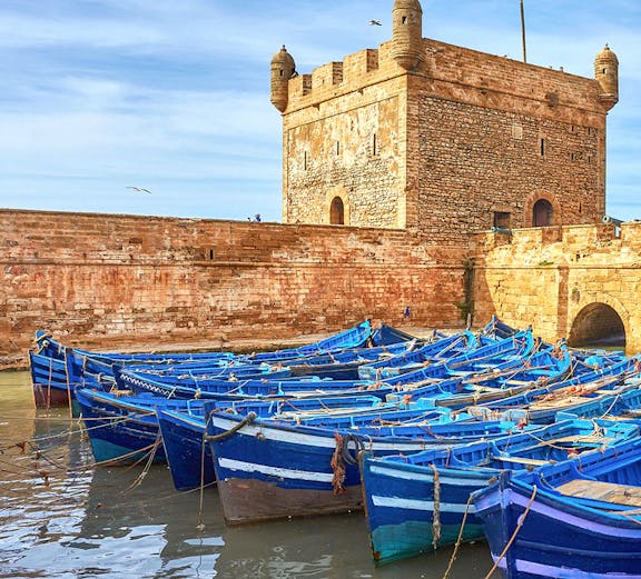 Blue fishing boats docked near Sqala du Port tower in Essaouira, Morocco.