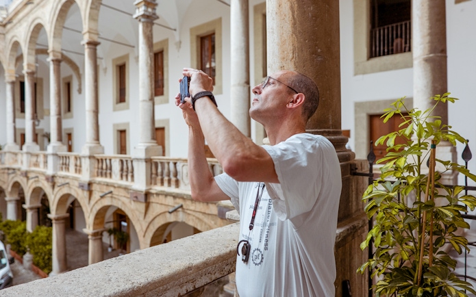 Visitor photographing the arches of Palazzo Dei Normanni during a guided tour.