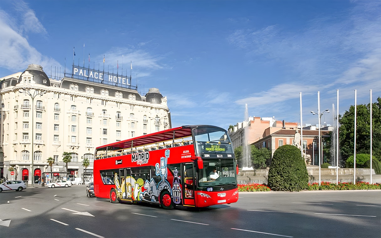 Hop-On Hop-Off bus near Royal Palace in Madrid cityscape.