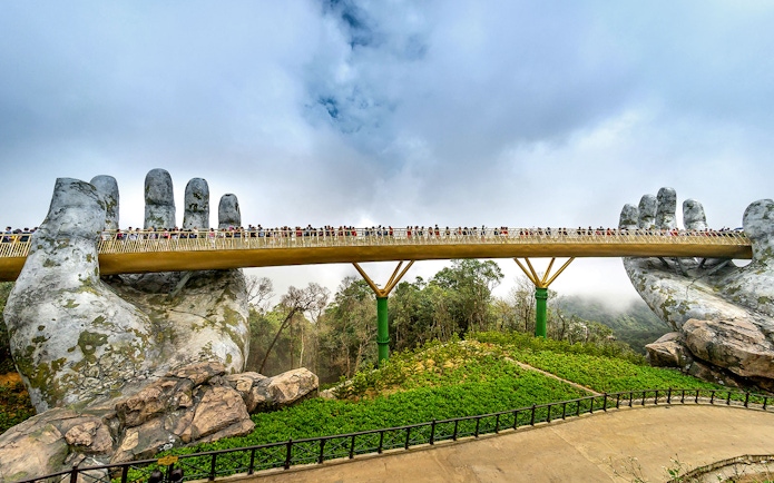 Golden Bridge in Da Nang held by giant stone hands, with tourists walking across.