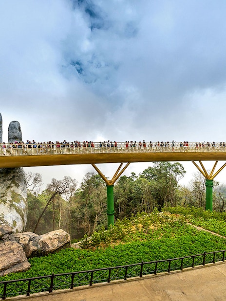 Golden Bridge in Da Nang held by giant stone hands, with tourists walking across.
