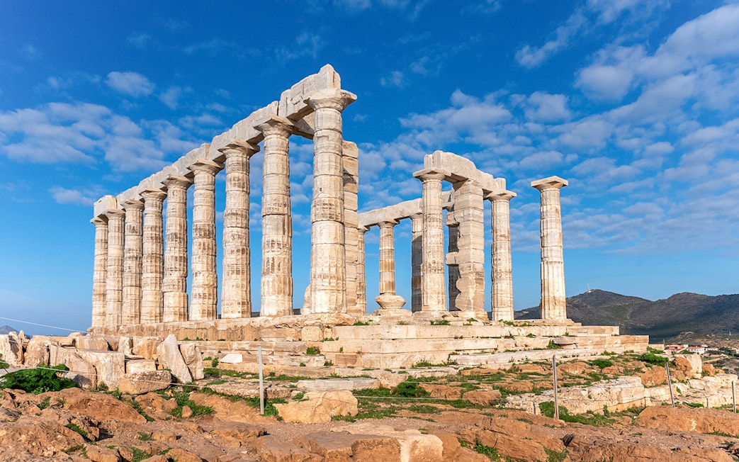 Temple of Poseidon ruins at Sounion, Attica, Greece under a blue sky.