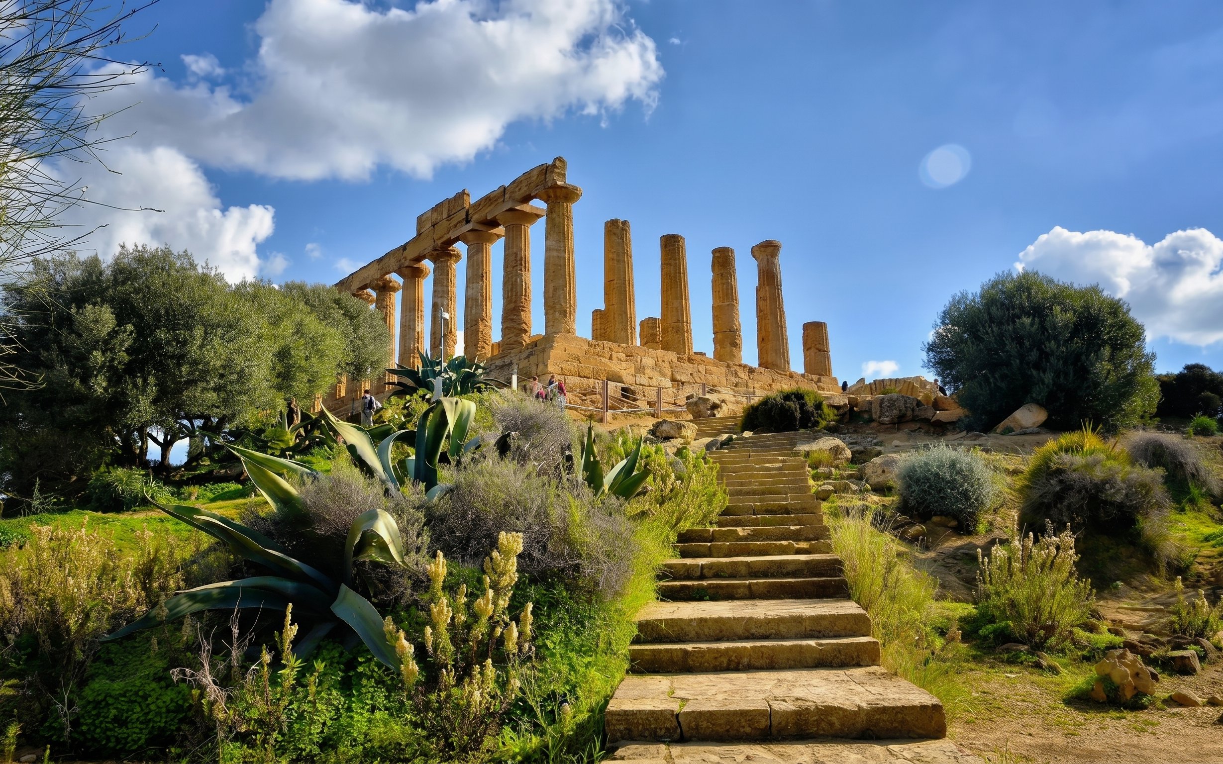 Ancient Greek temple ruins in Agrigento, Sicily, with stone steps and lush greenery.