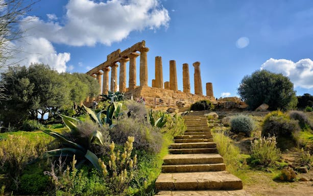 Ancient Greek temple ruins in Agrigento, Sicily, with stone steps and lush greenery.