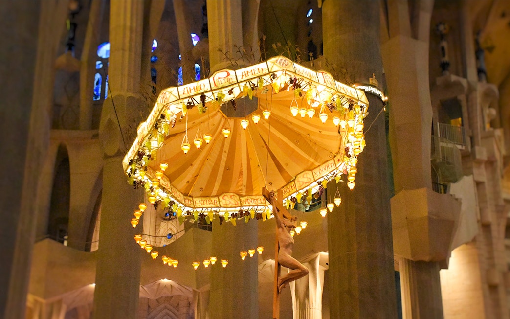 Jesus on cross beneath illuminated umbrella inside Sagrada Familia, Barcelona.